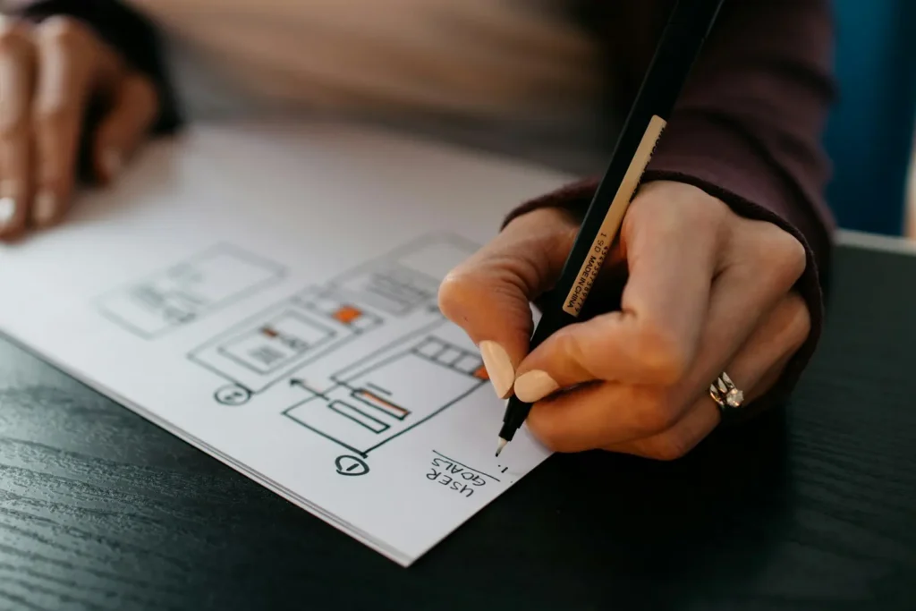 Les 10 pages indispensables d’un site vitrine — Aurea Media Main qui dessine au stylo la structure d’une page web sur une feuille