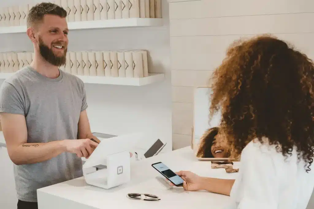 WooCommerce ou Shopify : que choisir pour votre boutique en ligne ? — Aurea Media Commerçant souriant qui encaisse une cliente avec un terminal de paiement